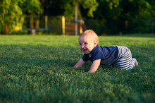 Baby Boy Is Crawling On A Green Lawn In Morning Sunlight.