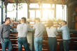 © DragonImages - Back view of men and woman gathering at bar counter in bright sunlight having meeting together