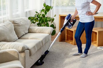 Wall Mural - Young woman in white shirt and jeans cleaning carpet with vacuum cleaner in living room, copy space. Housework, cleanig and chores concept