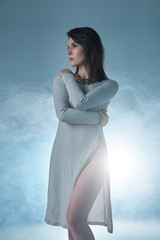 Woman portrait wearing a dress with a deep cut on smoky backgrou