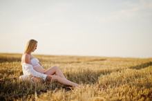 Blonde Pregnant Woman In Wreath Field At White Underwear Clothes On Sunset. Happy Moments Of Pregnancy.
