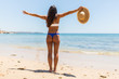 Woman on Beach standing with arms outstretched against turquoise sea. Rear view of female wearing bikini with raised hands. Carefree tourist is enjoying vacation at beach.