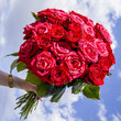 female hand holds a bouquet of red roses against the blue sky