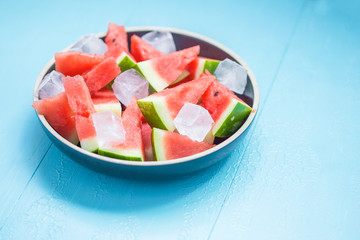 Wall Mural - slices of watermelon in a plate with ice on a blue background