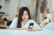 © Kanyanat - Beautiful Asian woman use of the smartphone sitting beside the bed.