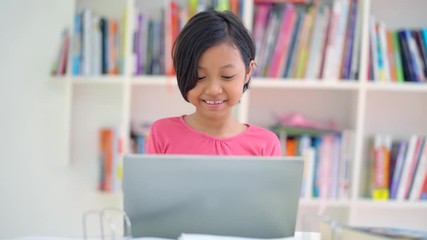 Wall Mural - Female elementary school student using a laptop computer while studying on the table in the library. Shot in 4k resolution