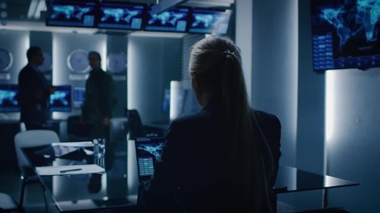 Wall Mural - Female Special Agent Works on a Laptop in the Background Special Agent in Charge Talks To a Military Man in the Monitoring Room. In the Background Busy System Control Center with Monitors.