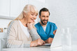 © LIGHTFIELD STUDIOS - smiling young caregiver and happy senior woman using laptop together