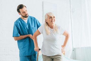 Wall Mural - male nurse supporting senior woman with walking cane