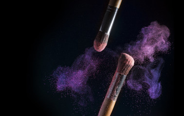 A splash of powder on a black background. Brushes for make-up on a black background. Explosion of make-up powder on tassels.