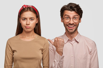 Wall Mural - Displeased European female being abused after quarrel with boyfriend who indicates at her with positive expression, dressed casually, isolated over white background. Two best friends indoor.