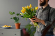 Man in grey shirt and with beard holding bouquet of yellow tulips