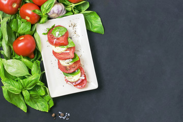 Caprese salad with mozarella cheese, tomatoes and basil on plate..Black background and copy space