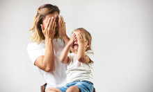 Little Girl Playing Peekaboo Game With Her Mother On White Background With Copy Space. Woman And Child Are Playing Peek-a-boo And Having Fun. Parenthood And Happy Moments Concept