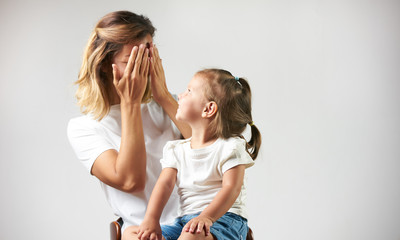 Little girl playing peekaboo game with her mother on white background with copy space. Woman and child are playing peek-a-boo and having fun. Parenthood and happy moments concept