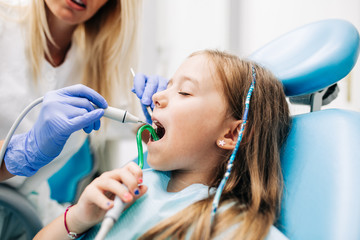 Wall Mural - Cute little girl sitting on dental chair and having dental treatment.