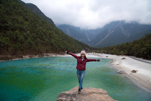Tourist Woman Standing On The Rock And Enjoy With Beautiful View Of Blue Moon Valley Land Mark In Yulong Snow Mountaind Natural Park In Lijiang City, China 