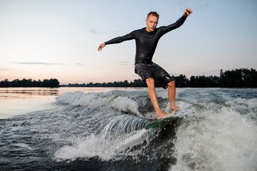 Wall Mural - Young man riding down the river on a wake board at the evening