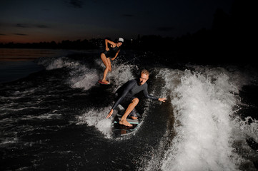 Wall Mural - Two wake surfers riding down the blue river at the evening