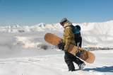 male mountaineer walks on snow with a snowboard in hands