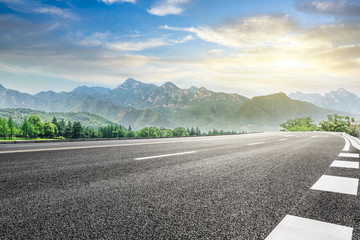 Empty asphalt highway and green mountain nature landscape at sunset