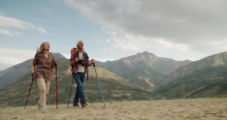 active senior caucasian couple hiking in mountains with backpacks, enjoying their adventure 4k