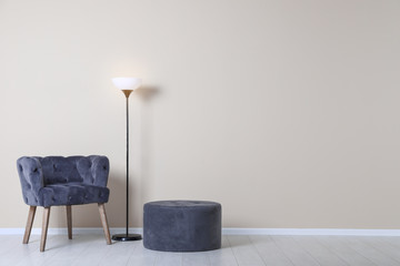 Poster - Comfortable armchair, pouf and lamp near color wall with space for text. Interior element