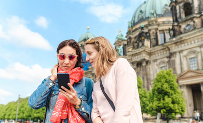 Two girl friends traveler using mobile phone app while walking at the city of Berlin. Wi-fi internet connection in Europe concept