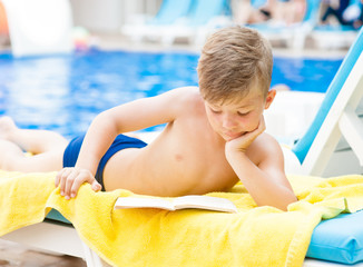 Wall Mural - Little boy is reading a book by the pool.  Relaxation resting vacations concept