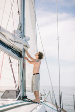 Young Hipster Sailor Man Adjusting Sails Of White Yacht Against Calm Blue Sea And Sky Background With Copyspace.