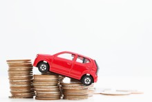 Little Red Car Over A Lot Of Money Stacked Coins With Isolated White Background . For Loans Costs Finance Concept. Empty Copy Space For Text.