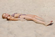 Young girl lying on the hot sand at sunset and sunbathing with her eyes closed