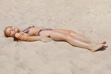 Young Girl Lying On The Hot Sand At Sunset And Sunbathing With Her Eyes Closed
