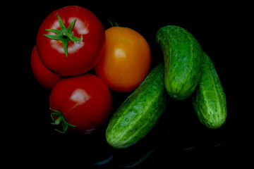 red and yellow tomatoes and green cucumbers lie on a black glass table