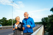 © hedgehog94 - Happy fit senior couple jogging along city bridge.
