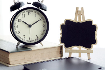 An alarm clock, books and black board over white curtain background