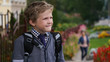 © cameravit - Little Caucasian curly boy in school uniform with backpack looking into the distance standing near school territory.
