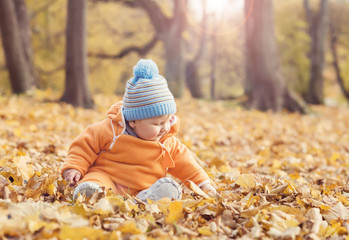 Happy toddler baby playing with leaves in autumn park.