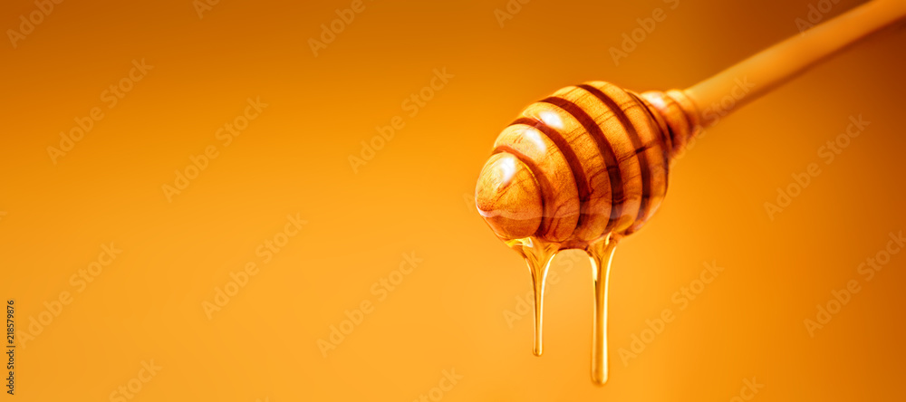 Honey dripping from wooden honey dipper over  yellow background. Sweet bee product for your design with copyspace. . - obrazy, fototapety, plakaty 