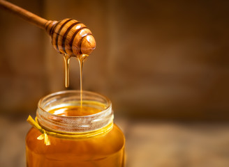 honey in a glass jar with honey dipper on rustic wooden table background. copy space.