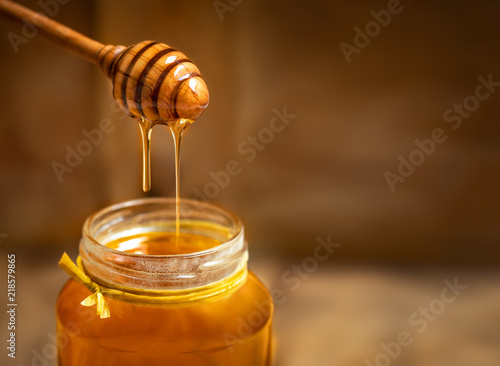 Photographie Honey in a glass jar with honey dipper on rustic wooden table background