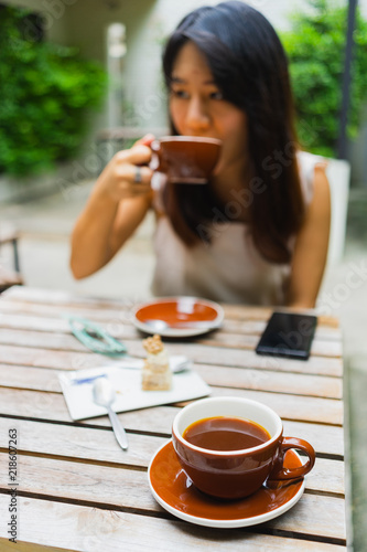 Fotografie, Obraz Hot americano coffee in the cup with Asian woman drink coffee in the coffee shop