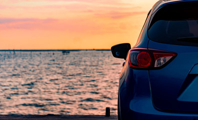 Blue compact SUV car with sport and modern design parked on concrete road by the sea at sunset. Environmentally friendly technology. Electric car technology and business. Hybrid auto and automotive.