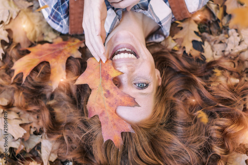 Fotografía young red hair beauty lying in orange autumn leafes