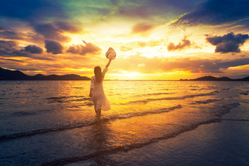 A lonely girl is walking along island coastline and has reflection on wet sand.