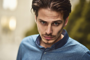 Young bearded guy with modern hairstyle looking at camera.