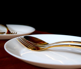 Closeup luxury golden forks and spoons in white dish on a dark wooden table on black classy background, dinner for two concept with copy space for text