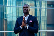 © yurakrasil - handsome Afro businessman in a stylish black suit looking into the sky and praying on street background office skyscraper. luck and successful deal concept