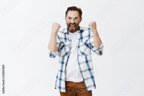 Excited Dedicated Football Fan Triumphing Joyfully Raising Clenched Fists And Yelling Yes Enjoying Great Match And Win Of Team Posing In Casual Outfit Over Gray Background Celebrating Success Buy This Stock