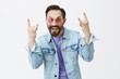 © Cookie Studio - I can still party and rock. Funny handsome adult male in trendy sunglasses and stylish denim jacket showing heavy metal sign and smiling joyfully, remembering youth while hanging out with son